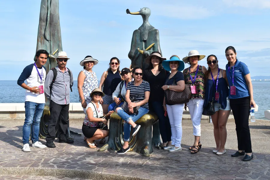 Grupo de viajeros junto a una escultura del Malecón de Puerto Vallarta con el mar al fondo.